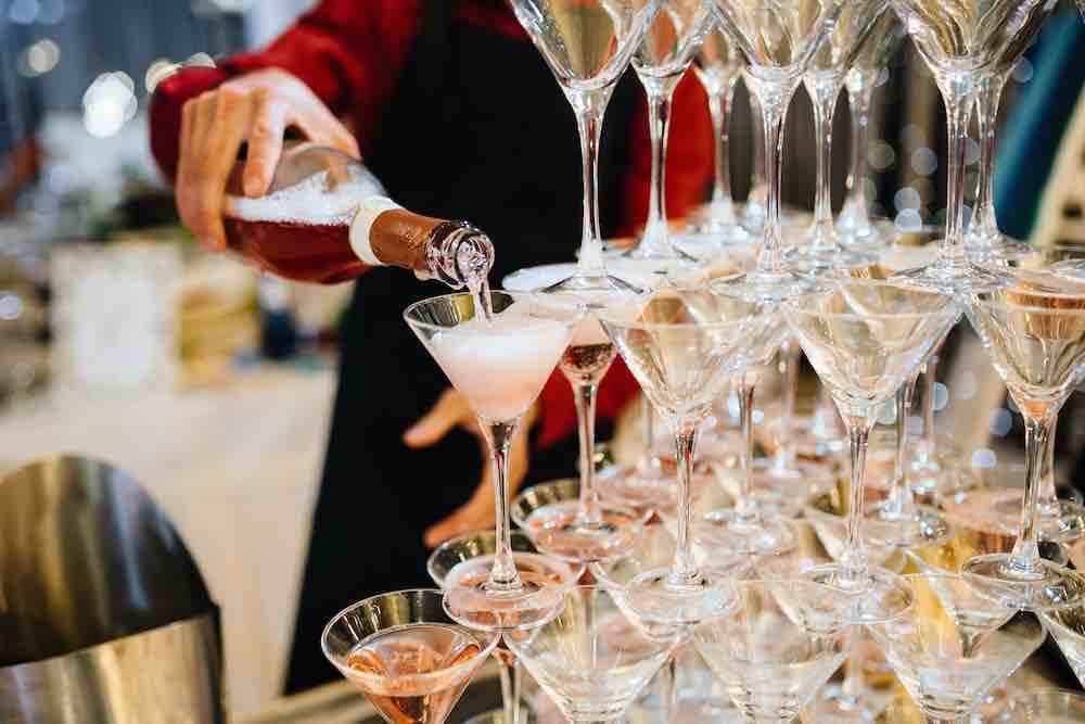 A man pours champagne into a tiered tower of glasses at a celebratory event.